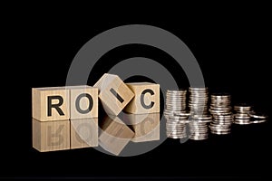 ROIC - text on wooden cubes on dark backround with coins. business concept