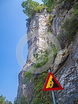 Roiling stones dangerous road. High cliffs and sign for falling rock pieces.