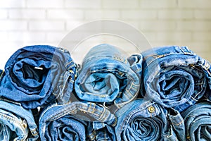 Roll blue denim jeans arranged in stack on wall background. Beauty and fashion clothing concept