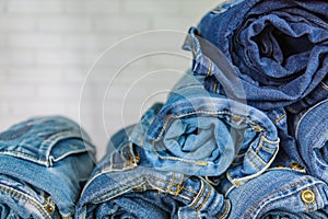 Roll blue denim jeans arranged in stack on wall background. Beauty and fashion clothing concept