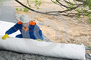 A roll of cloth to protect the surface of the soil, unwinding a worker in a blue uniform and a white helmet at a construction site