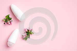 Roll-on deodorant bottles with blossom flowers on pink background. Flat lay, top view. Blank antiperspirant packaging, sweat