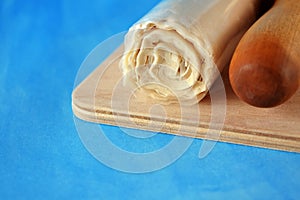 Roll of fillo dough and a rolling pin on a wooden board