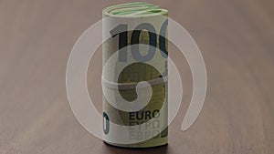 Roll of hundred euro bills on walnut table slide shot