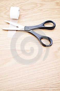 Roll of medical sticking plaster and pair of cutting scissors on a wooden table surface