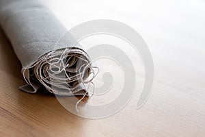 Roll of natural linen fabric with protruding threads on a wooden table