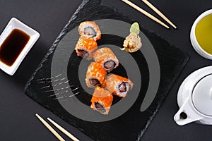 Roll with scallops and strawberries. Orange roll with tobiko caviar. The roll is served on a black shale with ginger and