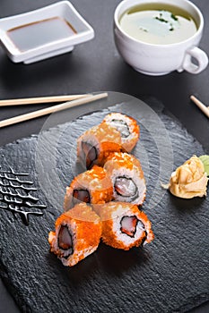 Roll with scallops and strawberries. Orange roll with tobiko caviar. The roll is served on a black shale with ginger and