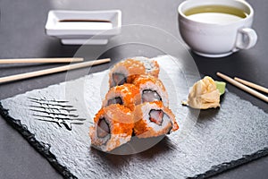 Roll with scallops and strawberries. Orange roll with tobiko caviar. The roll is served on a black shale with ginger and