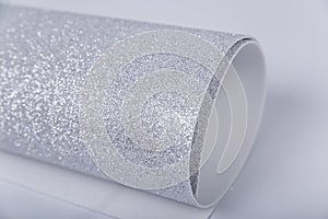 A roll of thick silver paper with glitter on a white background. Shiny fabric for creativity