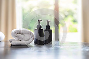 Roll up of white towels with shampoo bottles and liquid soap bottles on table with copy space on blurred room background. For