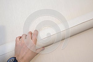 Roll of wallpaper in the hand of a worker on a wall background. Apartment renovation, construction work. Close-up