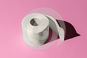Roll of a white toilet paper isolated on a pink background close-up. hard shadows from the sun at noon