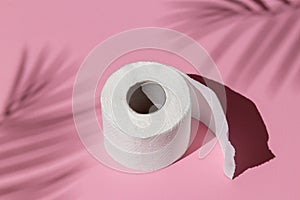 Roll of a white toilet paper isolated on a pink background under a palm tree shadow close-up. hard shadows from the sun at noon