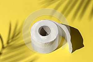 Roll of a white toilet paper isolated on a yellow background under a palm tree shadow close-up. hard shadows from the sun at noon