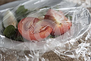 Roll of wrapping plastic stretch film over plate of vegetabes. Close-up isolated on wooden background. No plastic concept. Zero we