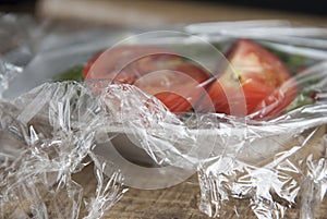 Roll of wrapping plastic stretch film over plate of vegetabes. Close-up on wooden background. No plastic concept. Zero we