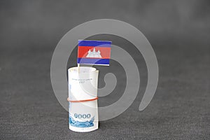 Rolled banknote money one thousand Cambodian Riel and stick with mini Cambodia flag on dark grey floor and background