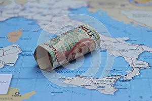Rolled banknote money one thousand Lire Italy put on the Italia map. Concept of currency or travel