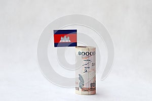 Rolled banknote money ten thousand Cambodian Riel and mini Cambodia flag on the white floor.