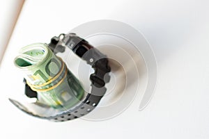 Rolled bundle of one hundred euro notes inside locked belt of modern wristwatch isolated on white background