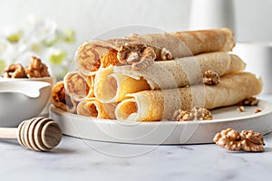 Rolled crepes or thin pancakes with honey and nuts on a white marble background. Maslenitsa or Pancake day traditional