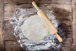 Rolled dough with rolling pin on wooden table covered with baking flour