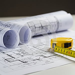 Rolled and flat architectural blueprints with technical drawings are visible on a white