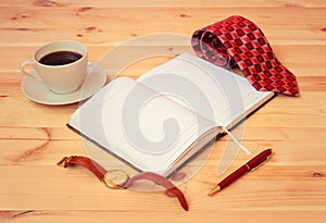 Rolled necktie, diary, watch, cup of coffee and pen on wooden table. Selective focus