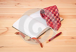 Rolled necktie, diary, watch and pen on wooden table. Selective focus