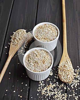 Rolled oats in bowls and spoons on dark wooden table background
