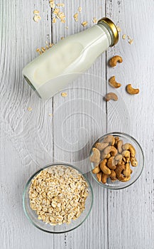 Rolled oats or oat flakes in bowl with oat milk and Cashew nuts on white wood background. Top view, Vertical. Healthy lifestyle,