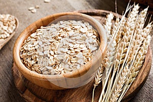 Rolled oats or oat flakes and golden wheat ears on wooden background.