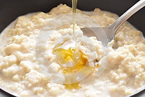 Rolled oats porridge with honey pouring.