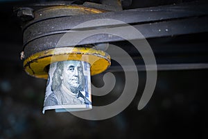 A rolled one hundred dollar bill close-up in a tractor engine pulley. Funding for agricultural land. The cost of maintenance and