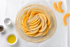 Rolled out dough with pumpkin filling surrounded by spices and olive oil on a white wooden background, top view