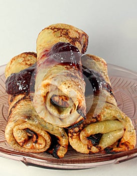 Rolled pancakes with strawberry jam on a glass plate photo