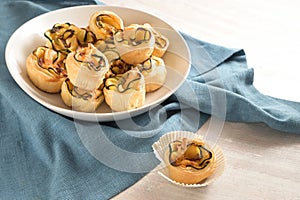 Rolled puff pastry muffins with zucchini slices, vegetarian finger food snack in a white bowl on a blue napkin for a warm or cold