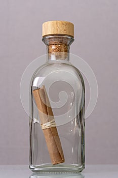 A rolled-up old paper note in a glass bottle with a cork on a light background. Concept: sea mail, a message from an island, a req