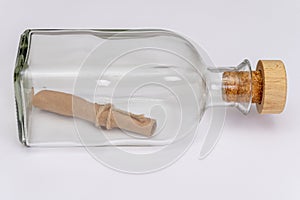 A rolled-up old paper note in a glass bottle with a cork on a light background. Concept: sea mail, a message from an island, a req