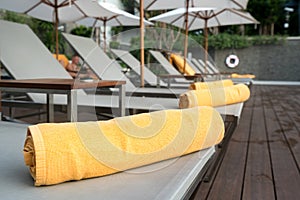 Rolled up orange towel on a sun lounger background of pool in re