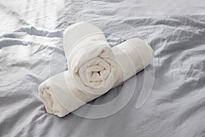 Rolled white clean towels on the bed with grey bedlinen.