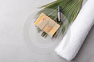 Rolled white pure cotton terry towel essential oil in dark bottle artisan Marseille soap palm leaf on gray stone background. Spa
