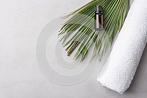 Rolled white pure cotton terry towel essential oil in dark bottle palm leaf on gray stone background. Spa wellness body skin face