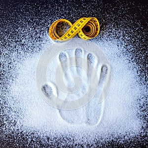 Rolled yellow tape measure and handprint on the scattered sugar.