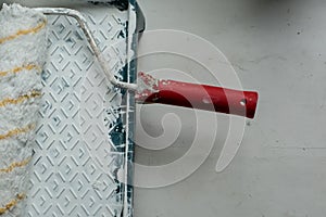 Roller with a red handle in a green pallet with white paint.