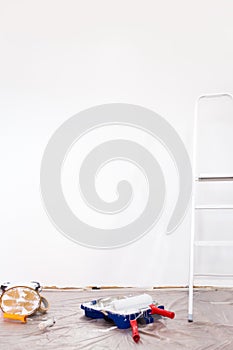 Roller, wall paint and ladder in front of a white empty wall