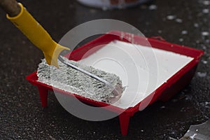 Roller in white paint. A painter applies paint to a roller with a handle