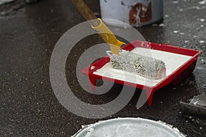 Roller in white paint. A painter applies paint to a roller with a handle