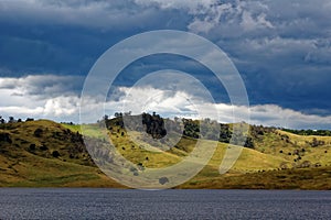 Softly undulating hills and patchy clouds at lake in Australian nature park